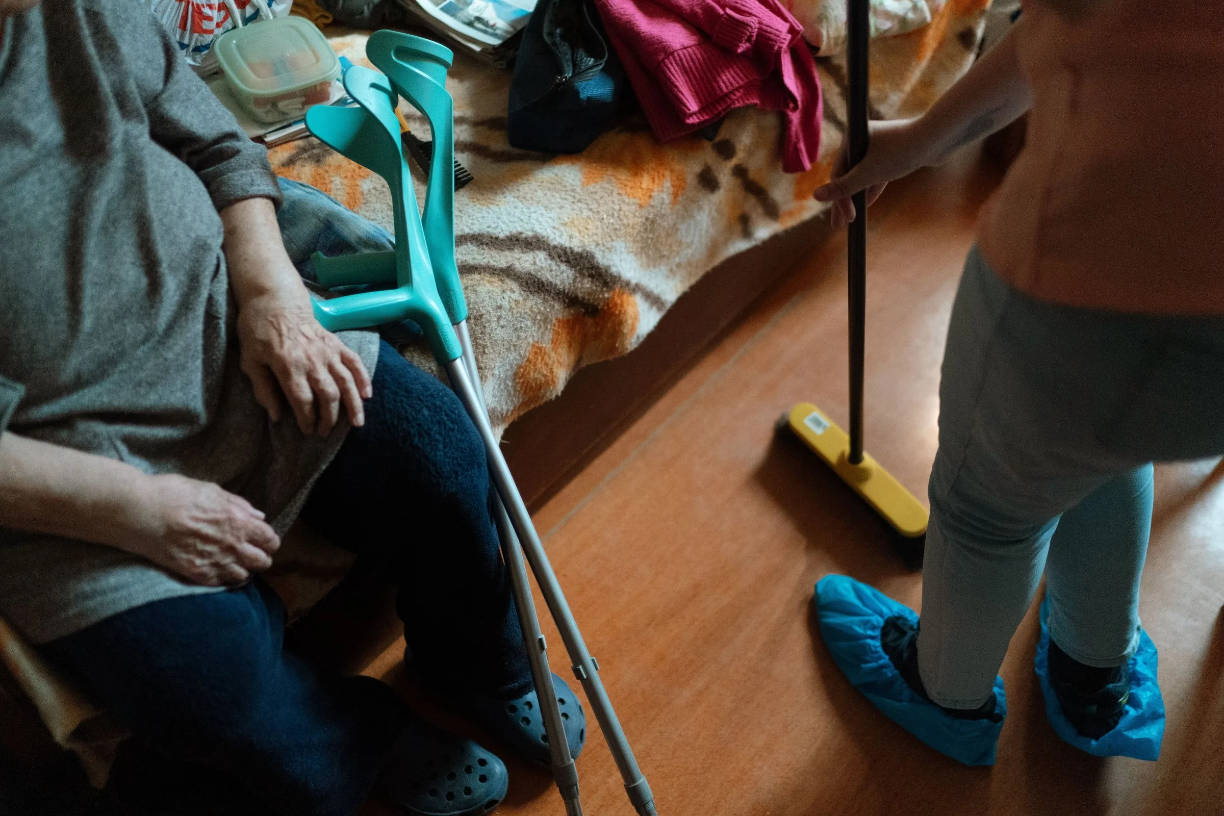 A caregiver providing light housekeeping while a senior rests nearby