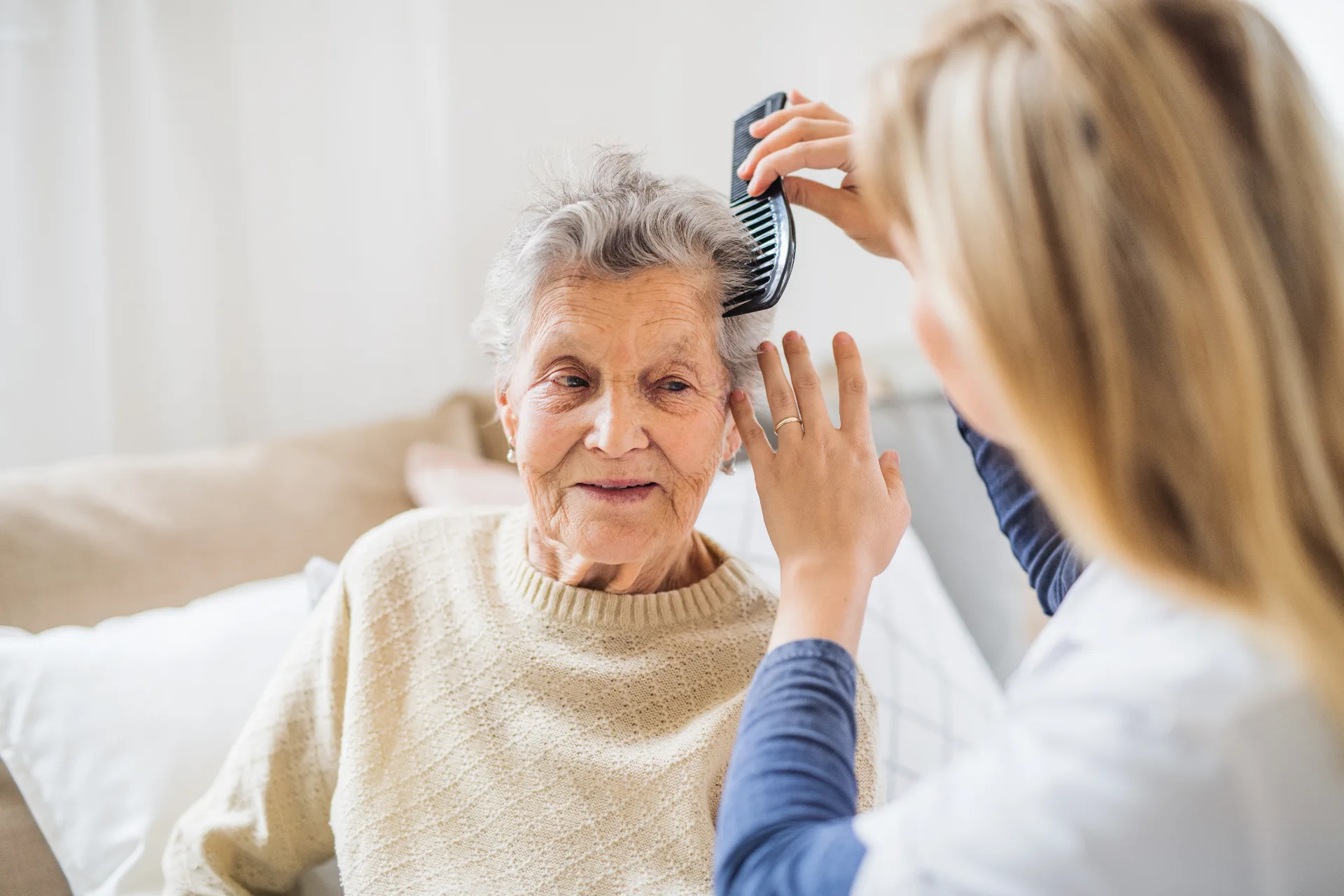 A caregiver gently helping a senior woman with personal grooming at home