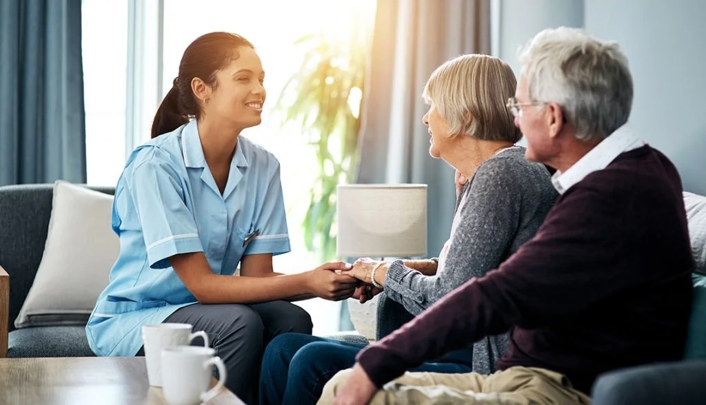 A professional caregiver speaking supportively with an older couple at home